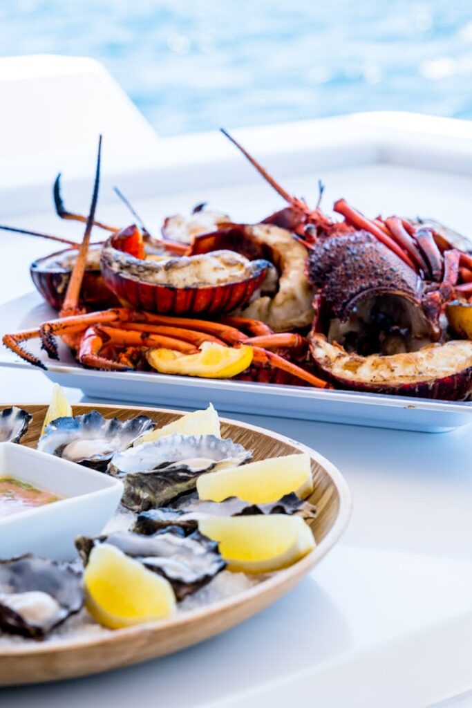 Close-up of a seafood platter featuring lobster, oysters, and lemon wedges on a table overlooking the ocean.